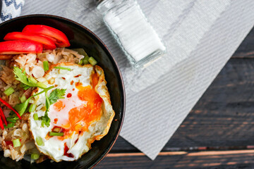 Japanese-style fried rice served in a black bowl with a fried egg and red tomato slices.
