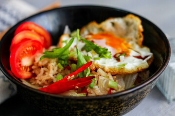 Japanese-style fried rice served in a black bowl with a fried egg and red tomato slices.