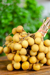 bunch of longan is placed on a wooden table with green leaves behind.