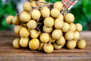 bunch of longan is placed on a wooden table with green leaves behind.