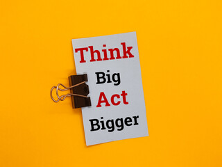 Paper clip with the concept of the word Think Big Act Bigger on a yellow background.
