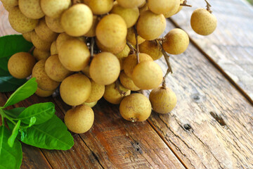bunch of longan is placed on a wooden table with green leaves behind.