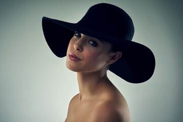 Shes got that beauty to cause a stir. Studio portrait of a beautiful young woman wearing a hat against a grey background.