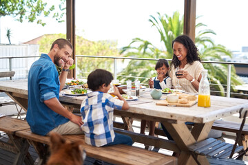 Meals always taste better when enjoyed with family. Shot of a beautiful young family enjoying themselves while having a meal together around a table outdoors.