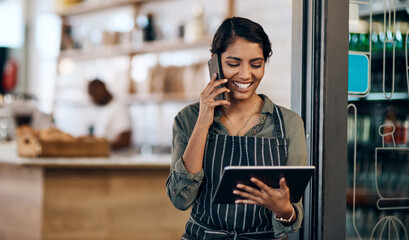 The wireless barista. Shot of a young woman using a digital tablet and smartphone while working in cafe.