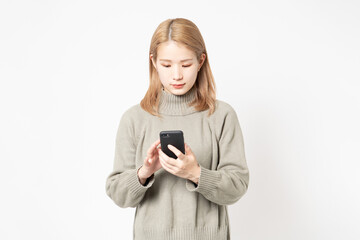 Fototapeta premium 白い背景の前に立ってスマホを使う若い女性