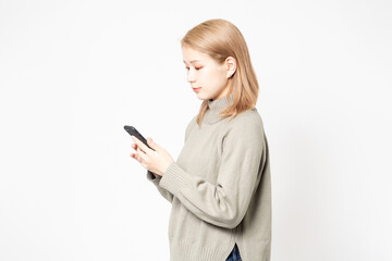 Naklejka premium 白い背景の前に立ってスマホを使う若い女性