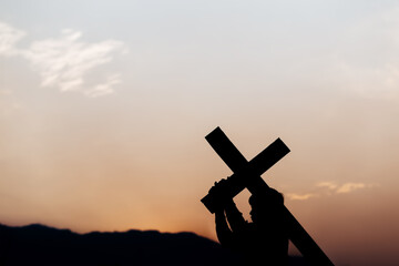 Silhouette of a man carrying a cross at sunset. concept of religion.