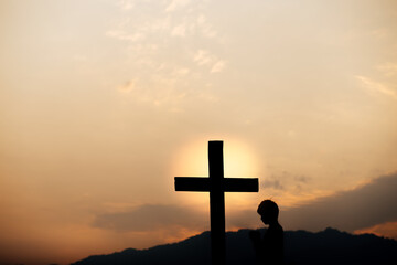 Silhouette of a man prayer in front of cross on mountain at sunset. concept of religion.