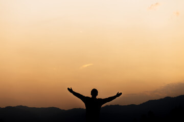 Silhouette of a man standing lift hands up and prayer and worship God at sunset. concept of...