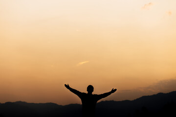 Fototapeta premium Silhouette of a man standing lift hands up and prayer and worship God at sunset. concept of religion.