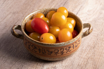small yellow tomatoes in a cup on wooden background