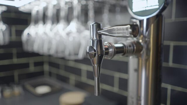 Close-up pan of metal tap for Estrella Galicia beer by glasses in bar