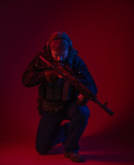 soldier in full gear with weapons. a man in headphones, body armor, with a backpack and a belt. red background. colored, blue-red light