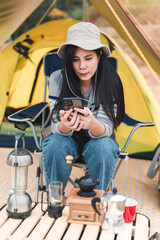 Fototapeta na wymiar Hipster asian woman camper using smartphone infront of camping tent on vacation.