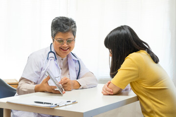 Asian girl and senior psychologist woman having therapy with digital tablet at clinic.