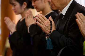 お葬式に参列する喪服の遺族（合掌・顔なし）
