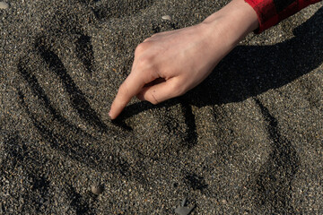 a hand draws some lines in the sand on the beach