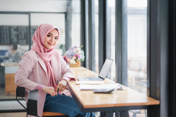 Confident muslim business woman working on laptop computer at co-working space. Looking and smiling into camera.