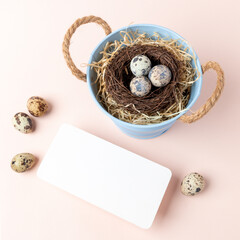Easter greeting card with nest of quail eggs in small bucket and empty white note on pastel pink.