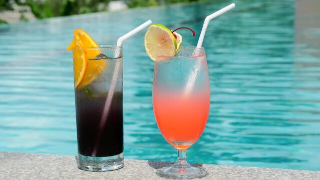 Vacation, summer, holiday, luxury resort concept. Two glasses with tropical cold cocktails with ice, plastic straw and slices of lime and orange near blue swimming pool in hot summer day