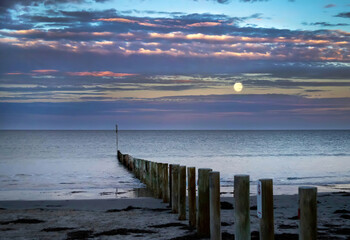 Sea landscape in the early morning on the beach with colorful clouds before sunrise with moon on the sky