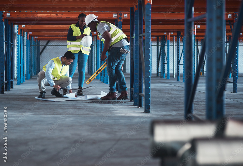 Wall mural We speak engineer fluently. Shot of a group of contractors using a blueprint to plan in the warehouse.