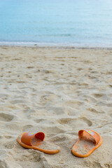 Fototapeta na wymiar Orange flip-flops on the sand in the beach with blue sea background.