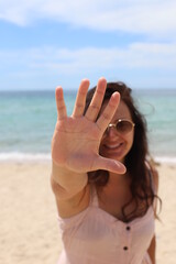 a girl on the beach covers the camera with her hand.