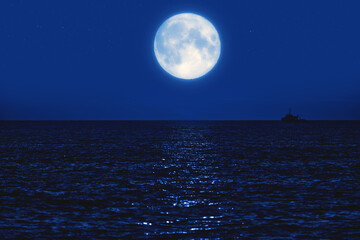 Full Moon rising above ocean horizon with boat silhouette.
