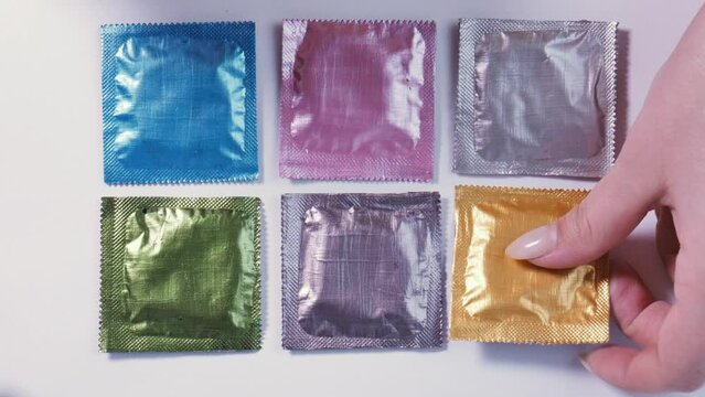Female hand chooses a condom among multi-colored packages and hides it in her purse. Safe sex planning, contraception, birth control, prevention of AIDS, gonorrhea, syphilis and STDs