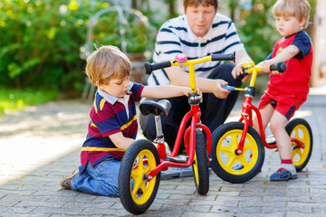 Two happy little kid boys and father repair chain on bikes and change wheel of balance bicycle