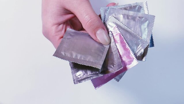 Women's hands choose a pink condom package among silver ones. Special sexual relationship.
