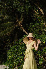 Beautiful young woman in long green dress and straw hat on Seychelles beach on Mahe or La Digue island