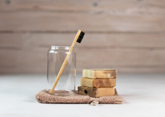 Bamboo toothbrush in a transparent glass and Homemade organic plant-based soap on a beige terry towel. Eco-friendly, biodegradable, zero waste.