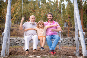 Fathers day. Grandfather with son and grandson swinging together in summer garden on swing outdoors. Active leisure for man family.