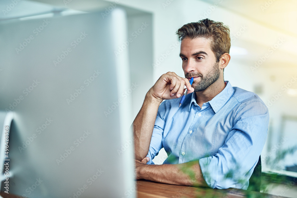 Poster thinking of some bright ideas. shot of a young businessman working on a computer in an office.
