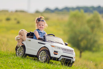 little girl rides on a children's car on a green lawn