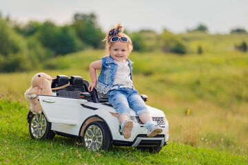 girl sits on the hood of a children's car that stands on the lawn