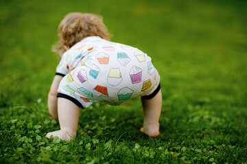 Cute adorable baby girl crawl and make first steps outdoors. Healthy happy toddler child learning...