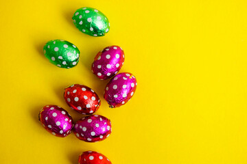 Chocolate egg in colorful foil for Easter on yellow background. The egg is wrapped in red foil. Happy Easter. Chocolate. Sweets for children and adults. Candy. Dessert. Copy space. Top view. Flat lay