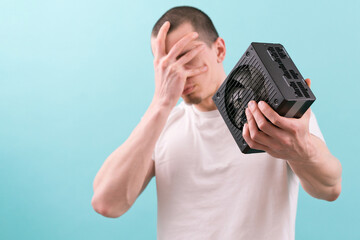 A sad man holds his head with a computer power supply in his hand on a blue background. Upsetting....