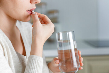 Young woman holding a glass of water and medication in the kitchen.
