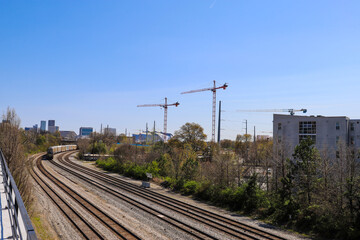 Fototapeta na wymiar long winding railroad tracks surrounded by lush green trees, buildings and tower cranes with skyscrapers and office buildings in the cityscape with blue sky in Atlanta Georgia USA