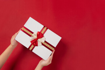 Top view of female hands holding gift or present box package on red  background