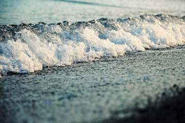 Sea wave wave in the rays of the daytime sun comes on the shore with pebbles. Nature and travel backgrounds