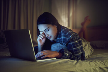 Its been a late night online. Shot of a sleepy young woman using a laptop late at night while lying...
