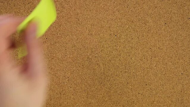 yeah. Stick the sticker on the cork board. Top view of note board. Wall of records in the office. Leave a reminder at work or at home. Caucasian male hand sticks and unsticks paper.