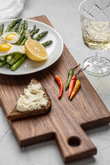 Fototapeta na wymiar On a wooden board is a plate with scrambled eggs, asparagus and olives. Nearby lies a toast with soft cheese