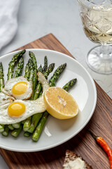 Vertical view dinner table with cutting board and plate full of asparagus with scrambled eggs and lemon and glass of white wine 
